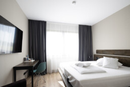 Standardzimmer Loftstyle Gerlingen - Doppelbett Tisch mit Stuhl und TV an der Wand